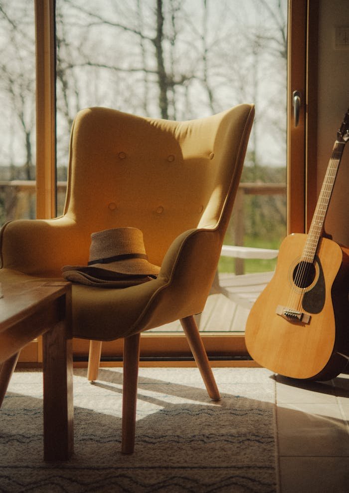 Warm, inviting interior with a yellow chair, a cowboy hat, and a guitar near a window.